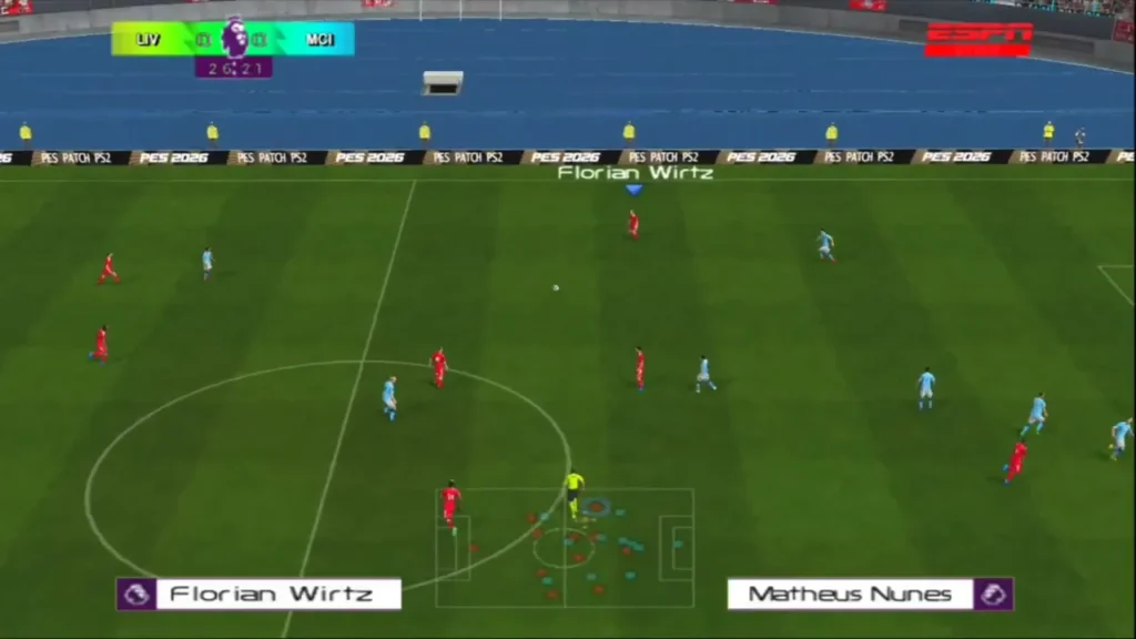 
Gameplay screenshot from eFootball PES 2026 PS2 ISO  (2025/26 Season Patch) showing a match between Liverpool (red kits) and Manchester City (light blue kits). The camera is in a broadcast top-down view at midfield, with the scoreboard showing LIV vs MCI at 26:21. Player names Florian Wirtz and Matheus Nunes appear on-screen, along with PES 2026 PS2 patch advertising boards around the pitch.
